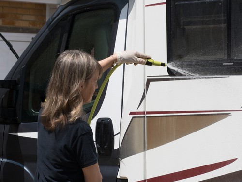 Lady washing an RV with a garden hose